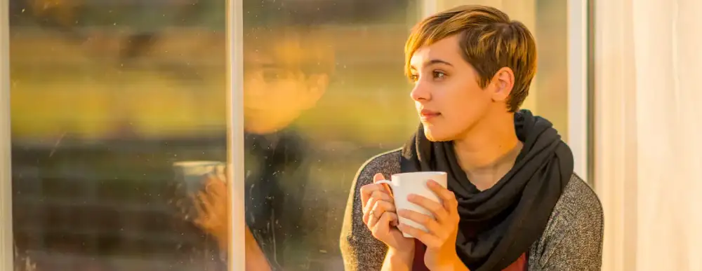 Woman at home, staring into the distance with a coffee cup