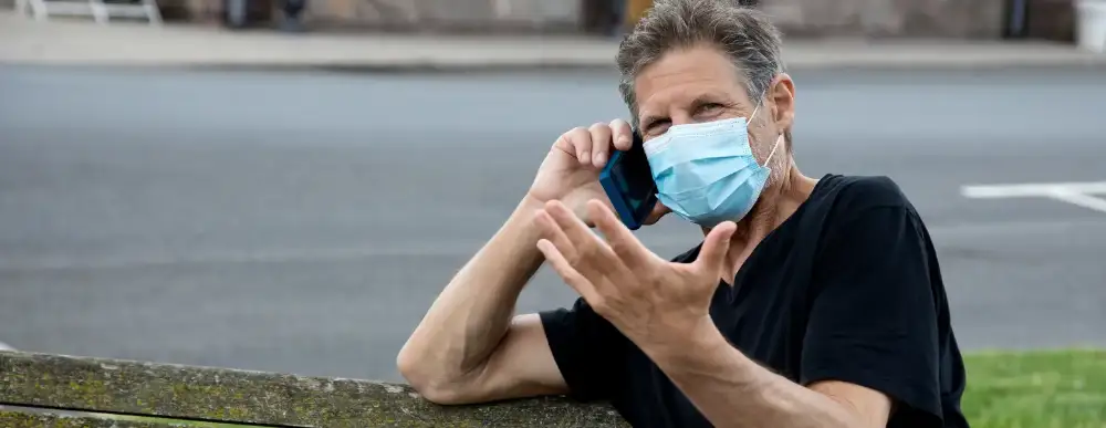 Man on the phone sitting on a bench with a mask