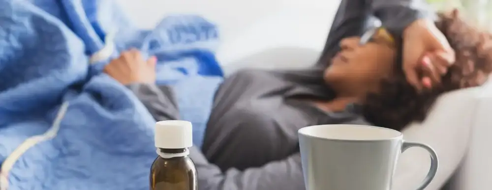 Woman laying on a couch at home with a bottle of medicine and a tea cup