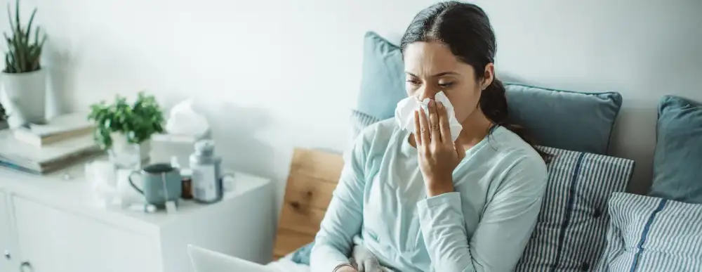 Woman sitting at home on her computer using a Kleenex