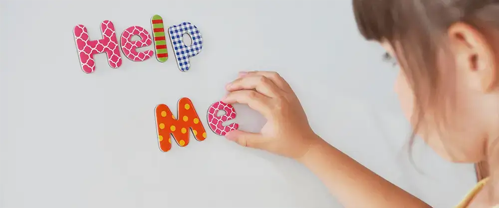 Photo of a little girl, creating words on a whiteboard it says help me