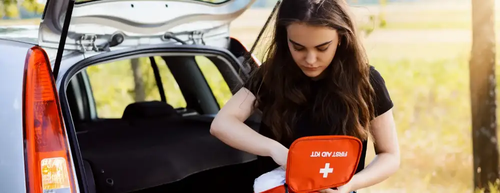 Woman sitting on the back of her car with a first aid kit