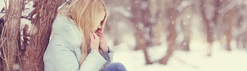 Woman sitting up against the tree in snow