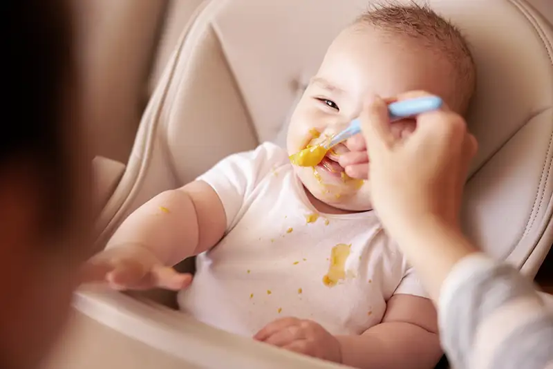 Mother spoon, feeding the baby in a highchair