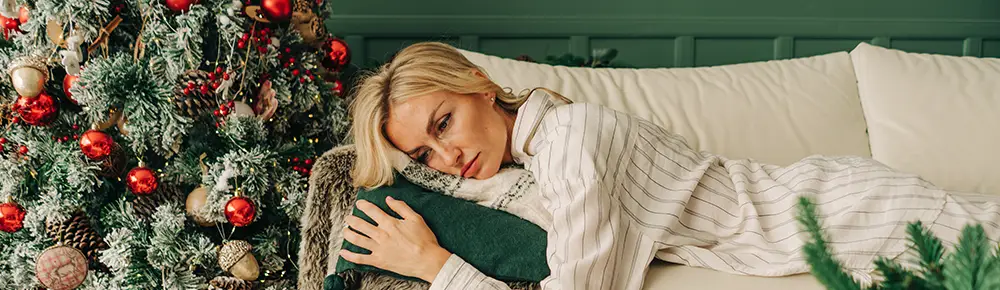 Woman laying on the couch next to a Christmas tree, indicating symptoms of holiday depression