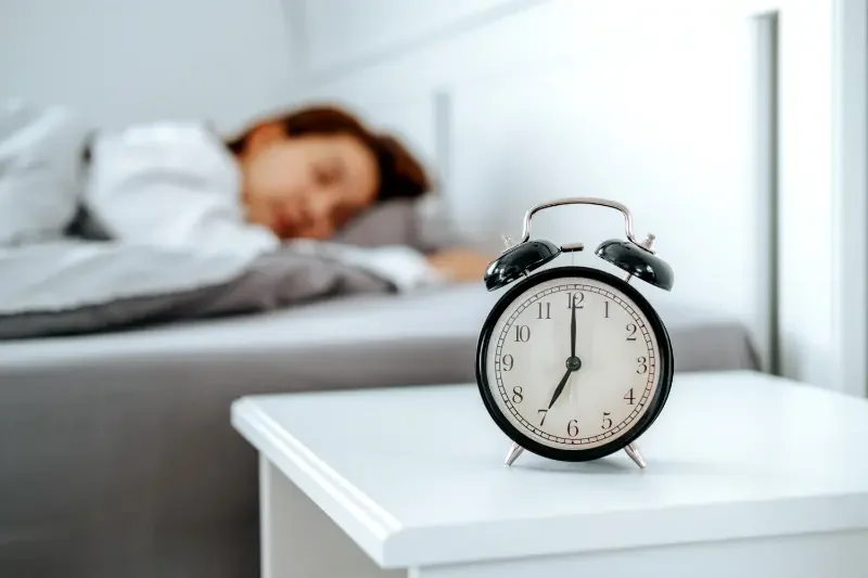 Alarm clock in the foreground woman sleeping in the background